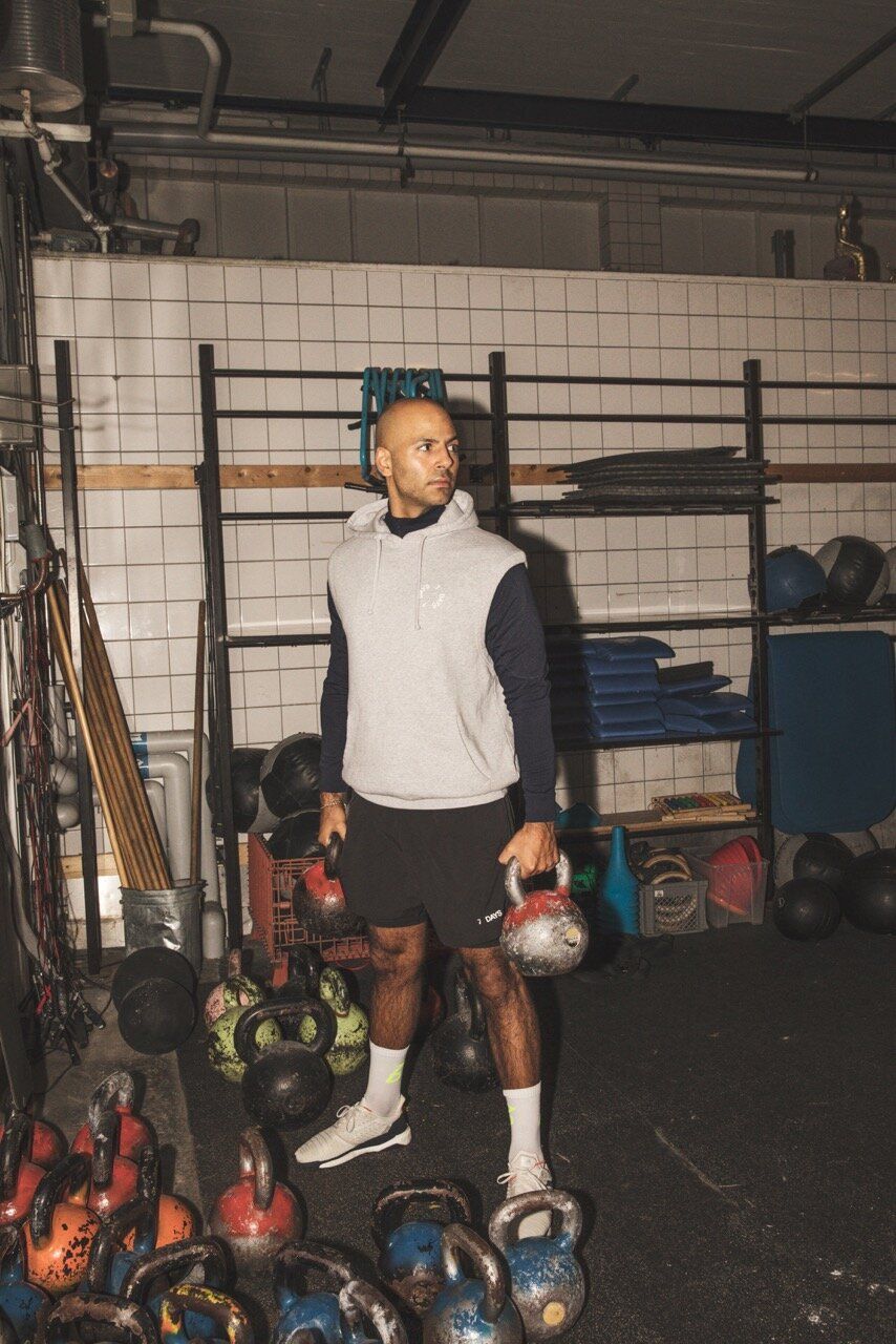 Mads Emil Møller stands in a gym, holding kettlebells, surrounded by fitness equipment.
