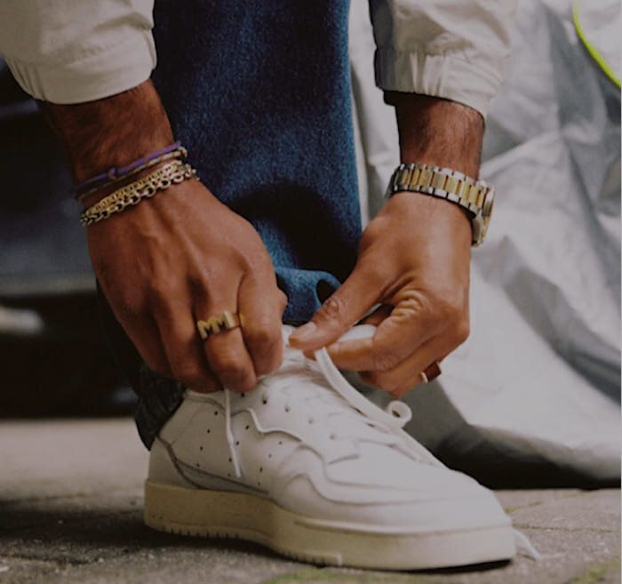 Mads Emil Møller tying shoelaces, wearing casual attire and accessories, outdoors.