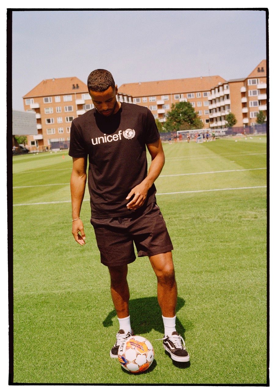 Mathias Zanka stands on a grassy field, wearing a UNICEF shirt and holding a soccer ball.