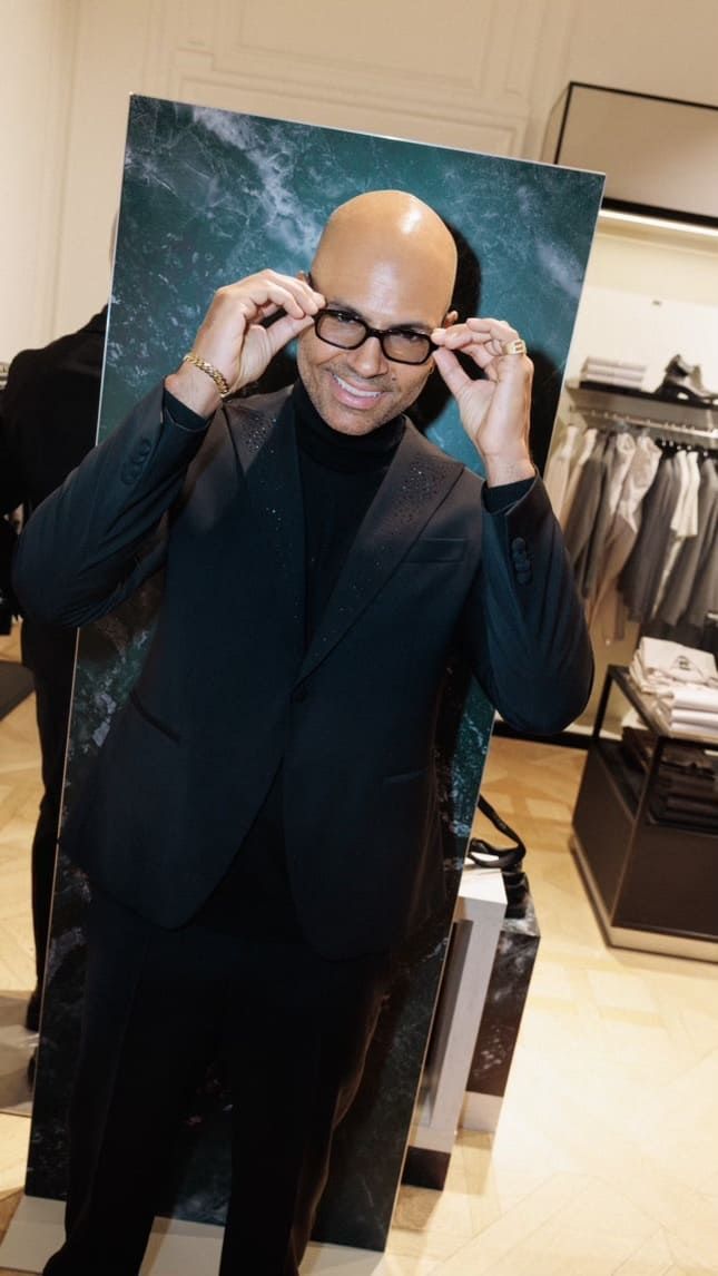 Mads Emil Møller adjusts his glasses, smiling in a stylish retail setting.