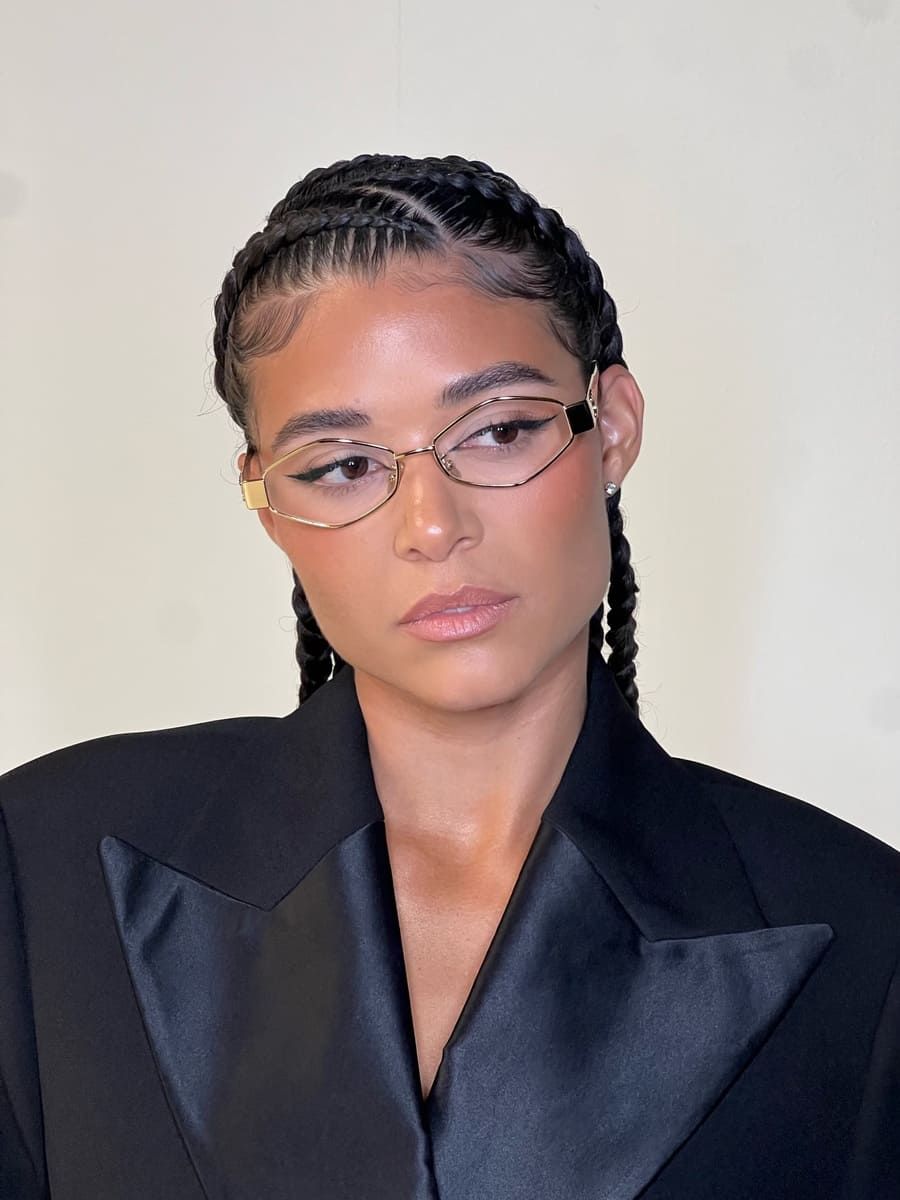 Cilia Trappaud poses in a black blazer, wearing glasses with braided hair against a neutral background.