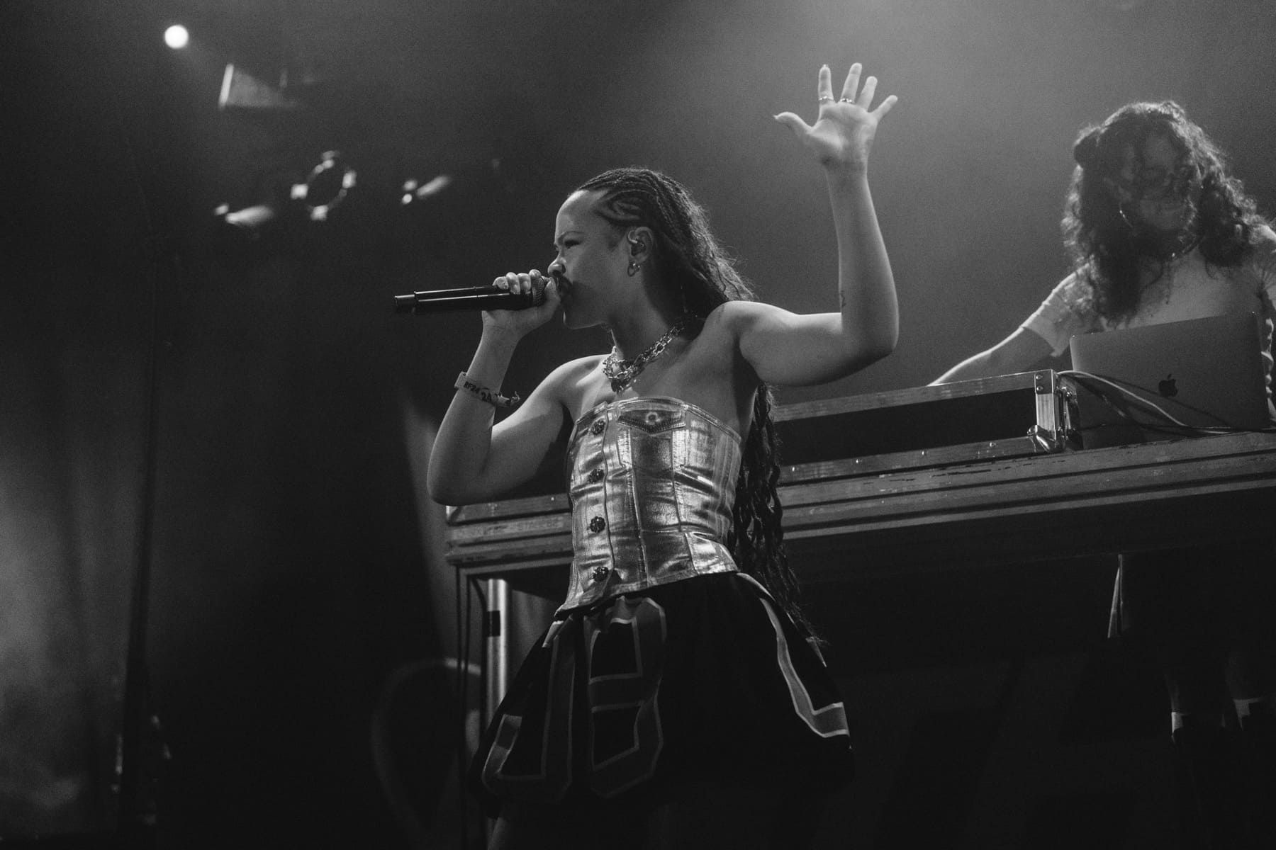 Bathsheba performs energetically on stage with a DJ in the background, illuminated by stage lights.
