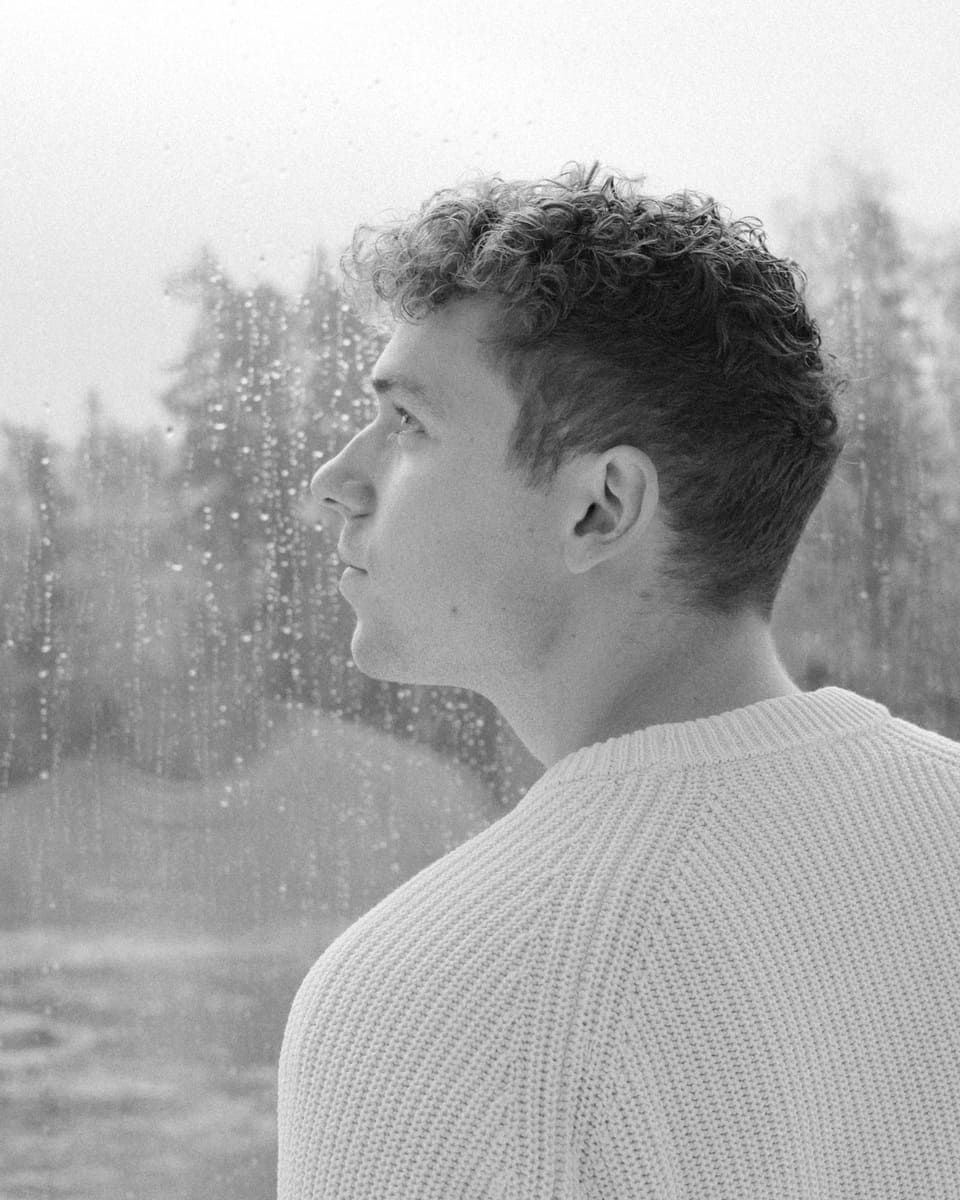 Rasmus Brohave gazes thoughtfully out a rain-speckled window, creating a contemplative mood.