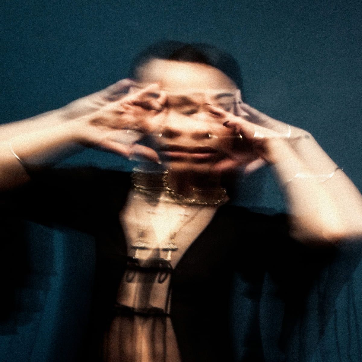Bathsheba poses with hands near her face, creating a blurred, artistic effect against a dark background.
